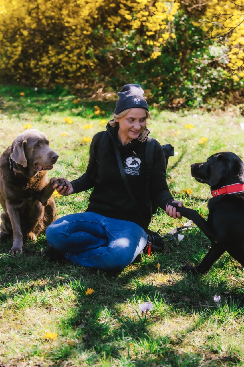 HeartcoredogsBerlin - Hundetraining - Magdalena lächelt inmitten von drei verschiedenfarbigen Hunden in einer verschneiten Umgebung